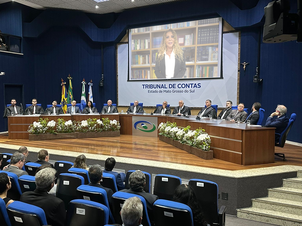 Palco de auditório com mesa de membros do TCE-MS e projeção da presidente do CNPGC ao fundo